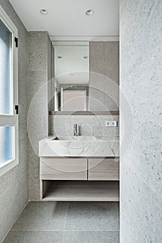 Toilet with light colored marble tiles, veined marble cabinet and low wooden drawers