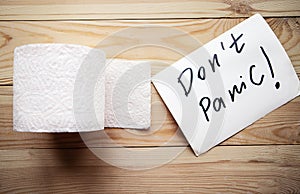 Toilet paper roll and message don`t panic on wooden background.