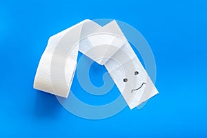 Toilet paper roll with painted face for proctology diseases concept on blue background top view