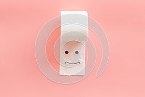 Toilet paper roll with painted face for proctology diseases concept on pink background top view