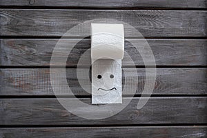 Toilet paper roll with painted face for proctology diseases concept on wooden background top view