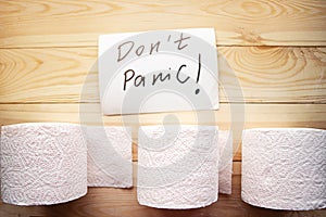 Toilet paper rolls and message don`t panic on wooden background.