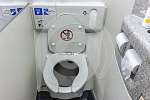 The toilet seat with the lid open at a aircraft lavatory. With a tissue dispenser and flush button above