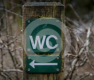 Toilet sign on a background of green trees in the forest. old WC sign