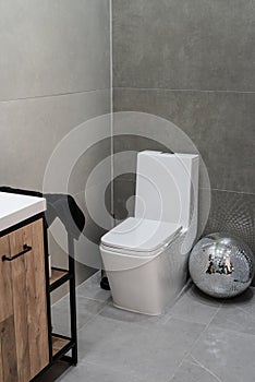 toilet and small washbasin in simple bathroom in gray floor and wall tiles