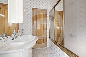 Toilet with white wooden bathroom cabinet with marble countertop and mirror with drawers, integrated lamps and shower cabin with