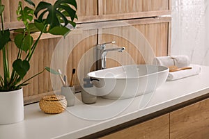 Toiletries and stylish vessel sink near wall in modern bathroom