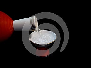 Pouring sake, liquor made from rice, from pottery choshi into a sakazuki or a cup on black background