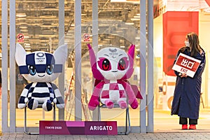 Staff of the olympics official shop holding an exit panel aside plushies of mascots saying arigato.