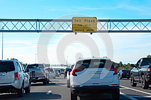 Toll Plaza 1/2 MILE yellow sign on overhead metal tri-chord truss with toll booths in the far distance and cars in traffic jam