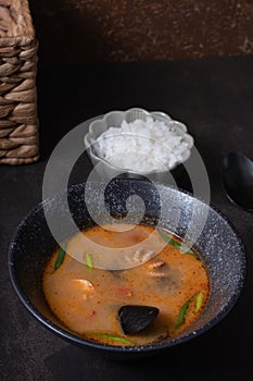 Tom yum soup with seafood and rice on dark background angle view