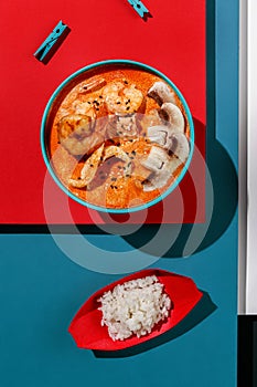 Tom yum soup with shrimps and rice in blue pastel color boul at blue and red background with sunlight and shadows, minimalism,top