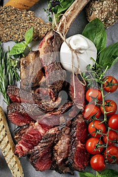 Tomahawk grilled steak cut into pieces with vegetables on a wooden Board