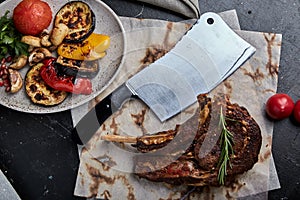 Tomahawk steak with vegetables and a knife on the table. Grilled meat with grilled vegetables and fresh vegetables on