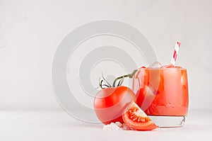 Tomato alcohol beverage in glass with ice cubes, tomato, straw, salt and juicy slice on white wood table, copy space.