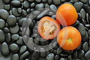 Tomato on black stone that has smooth glossy skin and round edge.