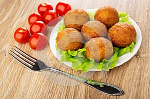 Tomato cherry, white plate with small fried pies on leaves lettuce, fork on table