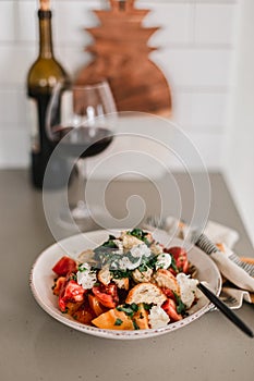 Tomato crostini salad with mozzarella cheese. Refreshing healthy dinner. Glass of red wine. Nourishing salad lunch. Panzanella