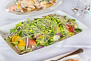 Tomato and cucumber salad with sunflower seedlings on a with plate.