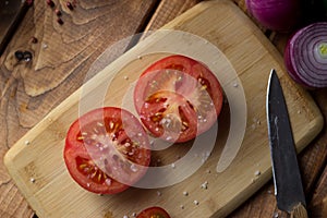 the tomato cut in half is sprinkled with large pieces of salt on a cutting board