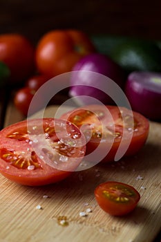 the tomato cut in half is sprinkled with large pieces of salt on a cutting board