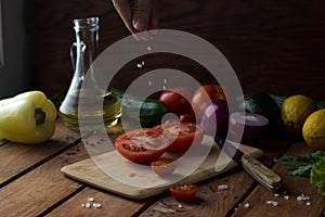 the tomato cut in half is sprinkled with large pieces of salt on a cutting board