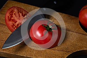 Tomato cut in half on a wooden cutting board. Tomato and knife on a dark background.