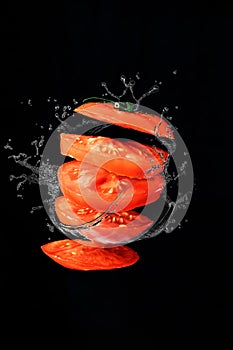 Tomato cut into pieces in the air on a black background, splashes of water and juice fly in different directions