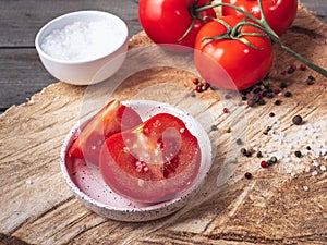 Tomato cut into slices on a saucer in the foreground, salt in a white vase, scattering of pepper.