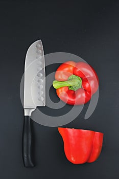 A tomato cut into two halves with a sharp knife. A Sharp knife and a tomato on black background on black surface