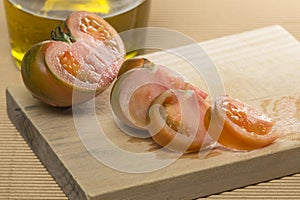 Tomato cut on wooden board, next to a porron of oil