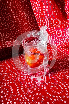 Tomato dropped in glass filled with water and printed red background