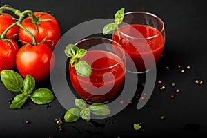 Tomato fresh juice with basil and cherry tomatoes on a black background