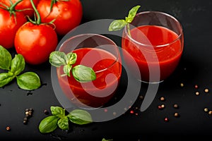 Tomato fresh juice with basil and cherry tomatoes on a black background. Close-up.