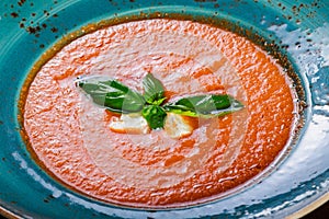 Tomato gazpacho soup in bowl with basil, feta cheese, ice on dark wooden background, Spanish cuisine.