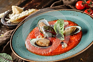 Tomato gazpacho soup with mussels, squid and cheese parmesan in plate over dark wooden background. Seafood, healthy food, close up