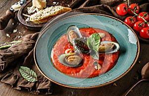 Tomato gazpacho soup with mussels, squid and cheese parmesan in plate over dark wooden background. Seafood, healthy food, close up