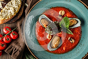 Tomato gazpacho soup with mussels, squid and cheese parmesan in plate over dark wooden background. Seafood, healthy food, top view