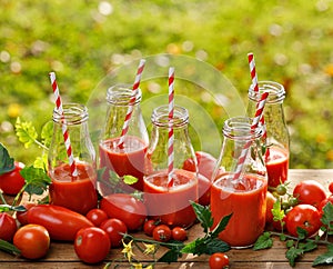 Tomato juice in glass bottles and fresh tomatoes on a wooden table