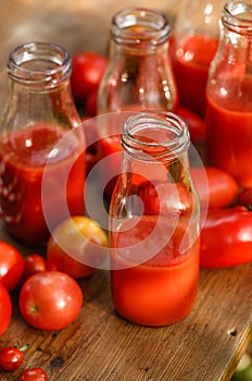 Tomato juice in glass bottles and fresh tomatoes on a wooden table