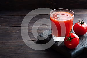 Tomato juice in glass glasses and fresh ripe tomatoes on a branch. Dark wooden background with copy space.