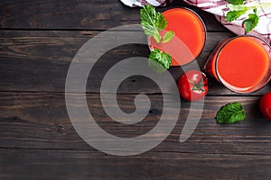 Tomato juice in glass glasses and fresh ripe tomatoes on a branch. Dark wooden background with copy space.