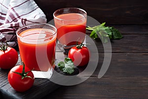Tomato juice in glass glasses and fresh ripe tomatoes on a branch. Dark wooden background with copy space