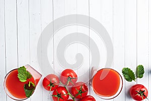 Tomato juice in glass glasses and fresh ripe tomatoes on a branch. White wooden background with copy space.