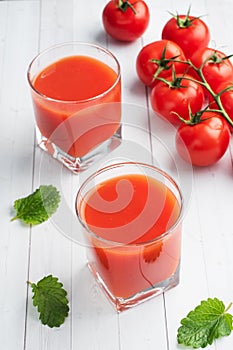 Tomato juice in glass glasses and fresh ripe tomatoes on a branch. White wooden background with copy space.