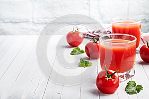 Tomato juice in glass glasses and fresh ripe tomatoes on a branch. White wooden background with copy space.