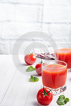 Tomato juice in glass glasses and fresh ripe tomatoes on a branch. White wooden background with copy space.