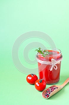 Tomato juice with a leaf of parsley in a glass jar, fresh tomatoes and a wooden spoon with pepper. Light green background, copy