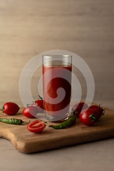 Tomato juice in a tall glass glass, cherry tomatoes, hot peppers on a cutting board, wooden background. Studio shot