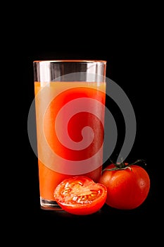 Tomato juice in a tall glass glass with natural fresh tomatoes on a black background